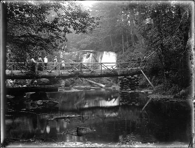 Historical photograph of Whatcom Falls with a log bridge in 1902, Bellingham, Washington. Photo by H. Ambrose Kiehl, public domain.